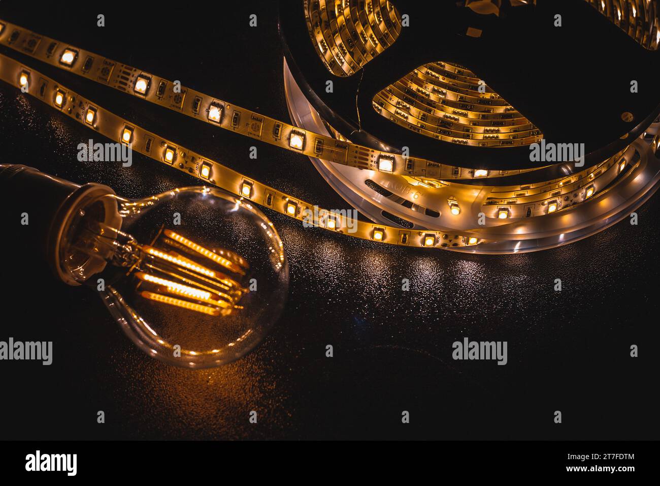 Mise au point douce de l'ampoule transparente placée sur la table noire près de la bande LED jaune incandescente Banque D'Images