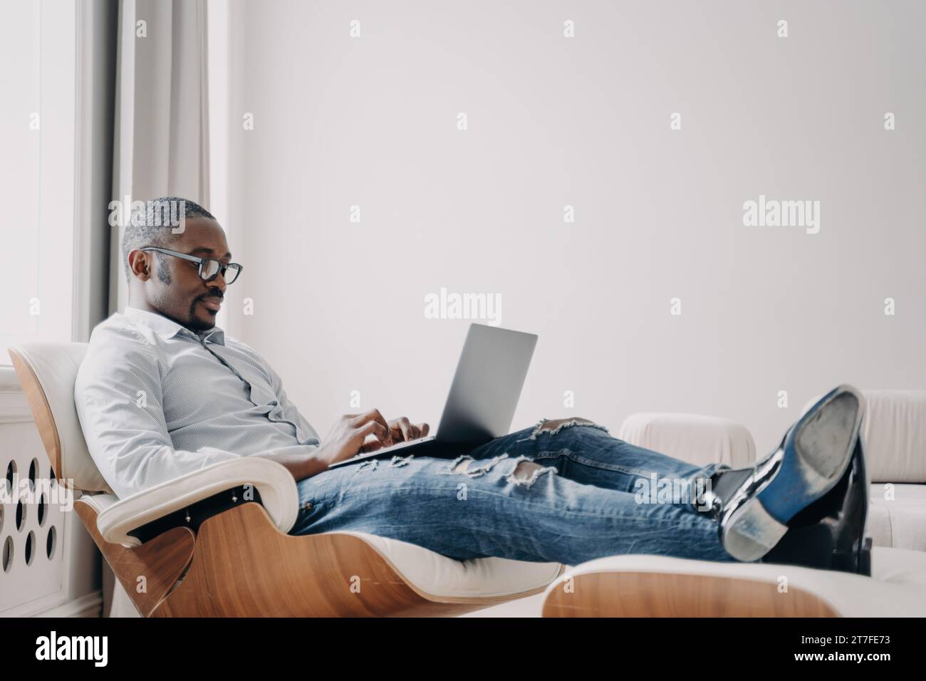 Homme d'affaires détendu dans des lunettes à l'aide d'un ordinateur portable, confortable dans une chaise moderne Banque D'Images