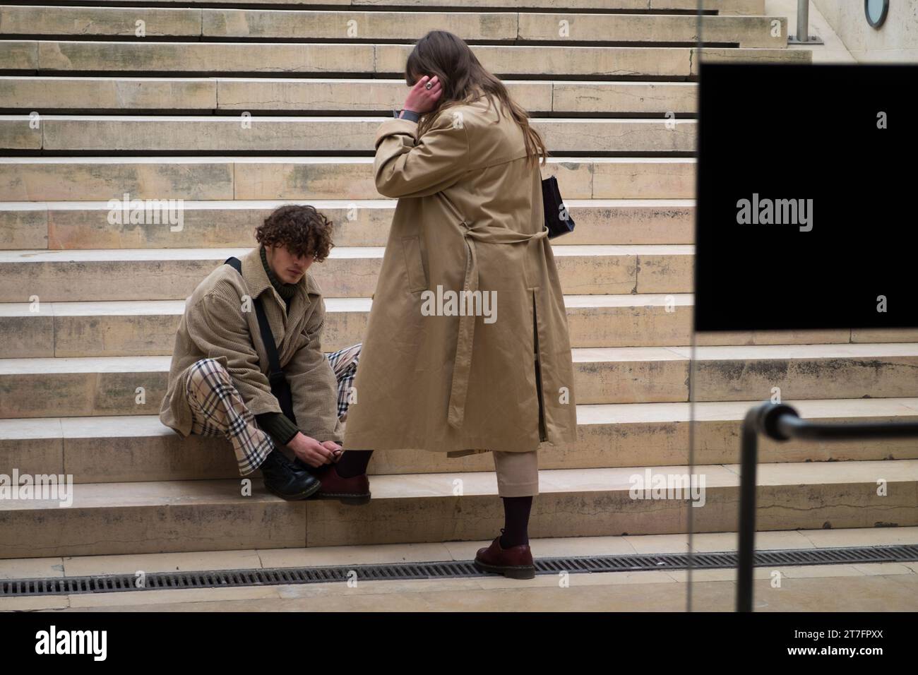 Jeune homme attachant gracieusement les chaussures d'une fille sur les marches du Louvre. Banque D'Images