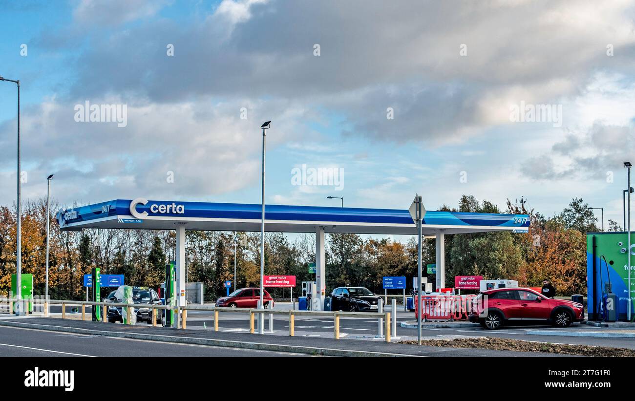 Station essence Certa avec pompes à carburant et points de recharge pour véhicules électriques, fonctionnant 24/7 sous un ciel nuageux, avec plusieurs voitures ravitaillées ou garées. Banque D'Images