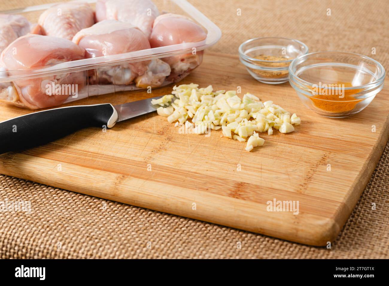 Ail haché sur une planche à découper en bois sur une table de cuisine gros plan. Recette de pilons de poulet marinés Banque D'Images