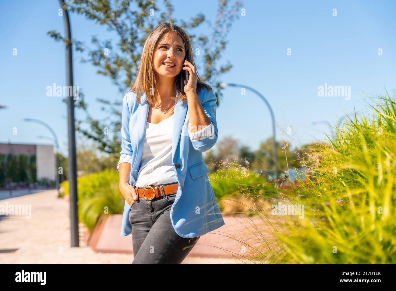 Élégante femme décontractée parlant à l'extérieur mobile à côté des jardins urbains Banque D'Images
