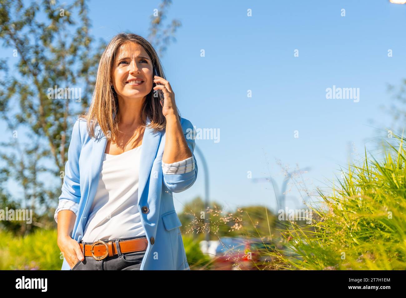 Fière femme d'affaires occasionnelle parlant au téléphone debout sur un quartier urbain résidentiel Banque D'Images