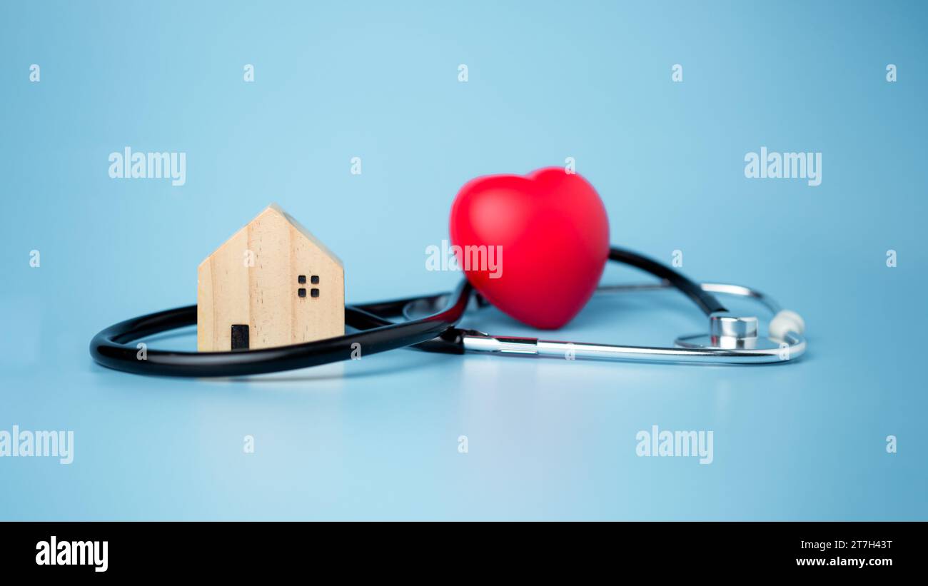 Concept d'assurance maladie et de bien-être médical, petite maison en bois et coeur rouge avec stéthoscope sur fond bleu, assurance maladie et accès à Banque D'Images