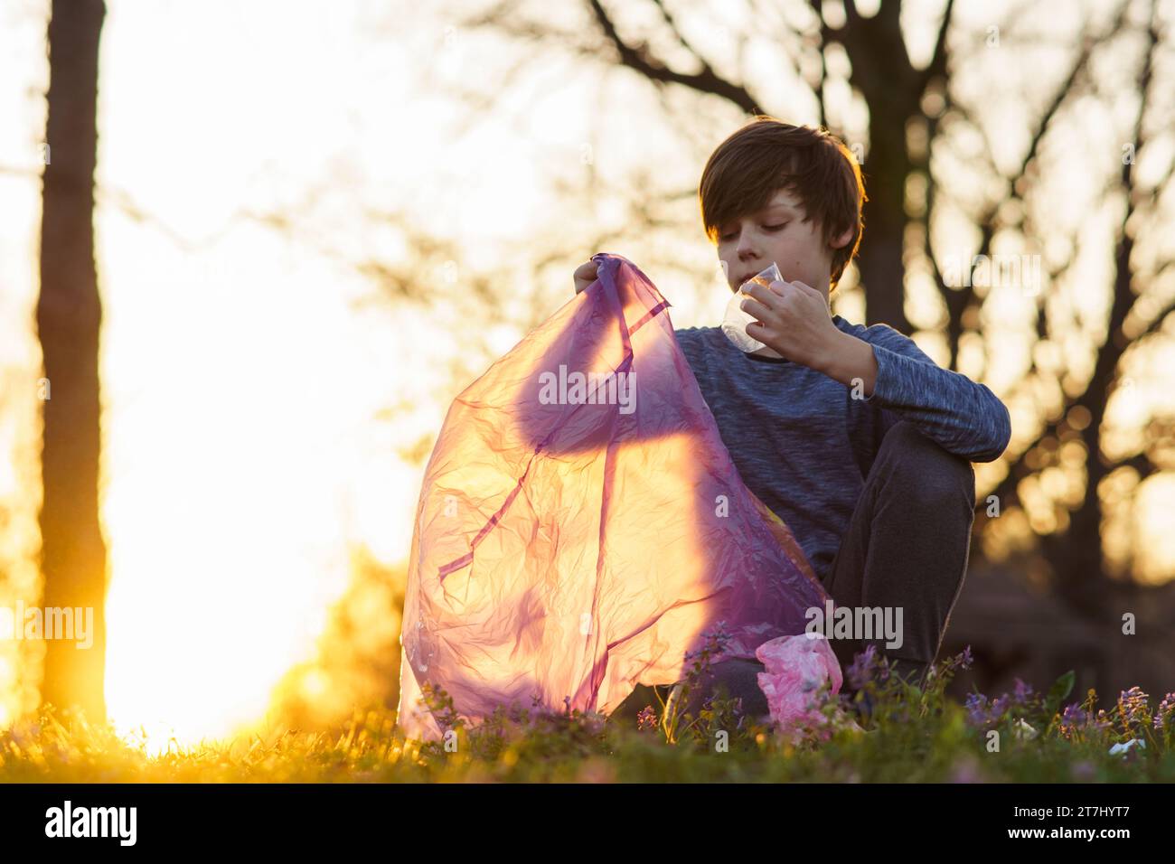 Mignon adolescent recueille les ordures dans le grand sac rose dans la nature, dans la prairie le soir d'automne au coucher du soleil. Problèmes environnementaux. Nous prenons soin de la nature. Sa Banque D'Images