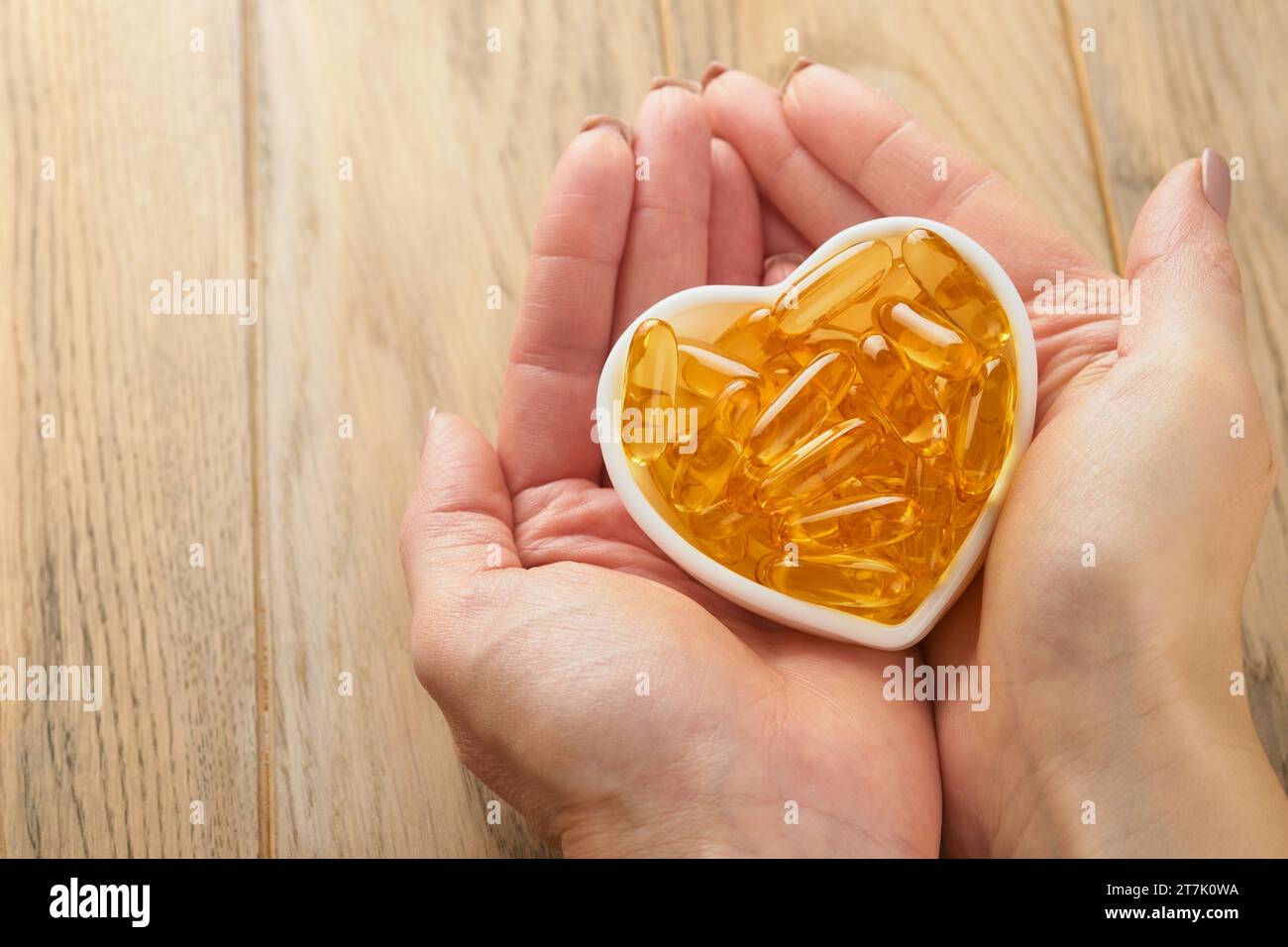 Femme ou médecin tient dans la main des capsules avec de la vitamine D, E ou des acides gras oméga 3,6,9 dans un bol en forme de coeur. Huile de poisson remplie d'huile de complément alimentaire. Naturel Banque D'Images