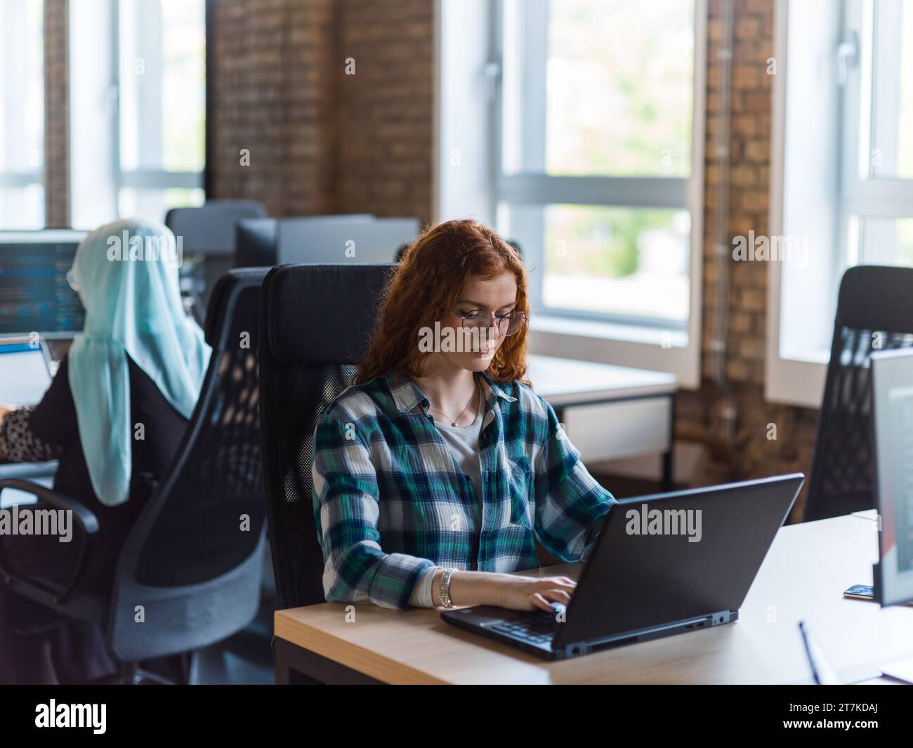 Une jeune femme d'affaires prospère aux cheveux orange vif s'engage dans un travail ciblé au sein d'un bureau moderne, mettant en valeur sa confiance et son dynamisme Banque D'Images