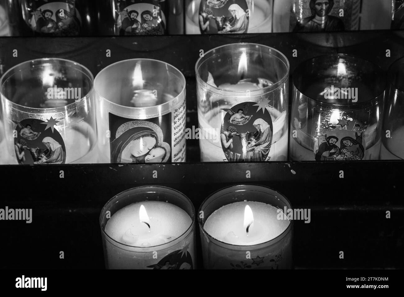 Sélestat, France - 25 décembre 2022 : les bougies de prière catholiques, avec la Sainte famille et Marie avec l'enfant Jésus, brillent dans l'église la veille de Noël. Noir blanc Banque D'Images