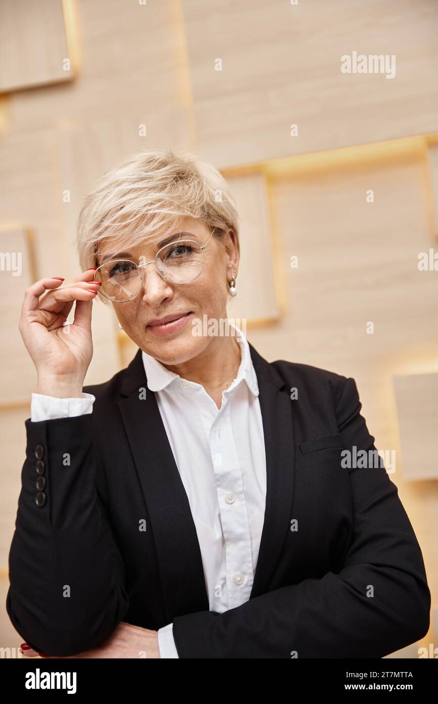 heureux blonde moyen agent immobilier dans des lunettes travaillant dans le bureau immobilier, regardant la caméra Banque D'Images