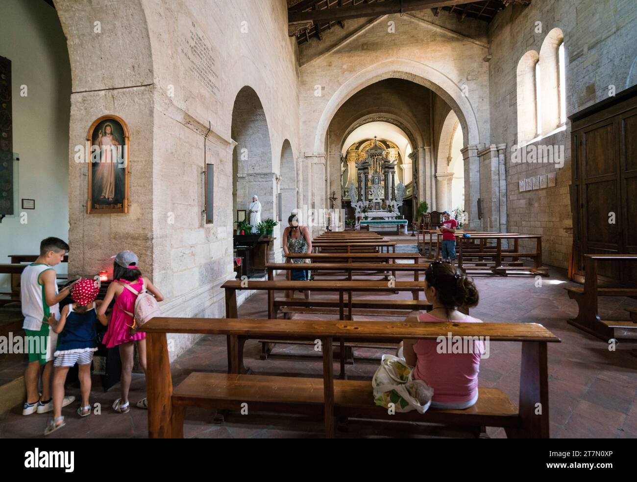 San Quirico, Italie : les enfants allument des bougies à l'intérieur de l'immense Collegiata di San Quirico romane qui a été rénové au 12e siècle Banque D'Images