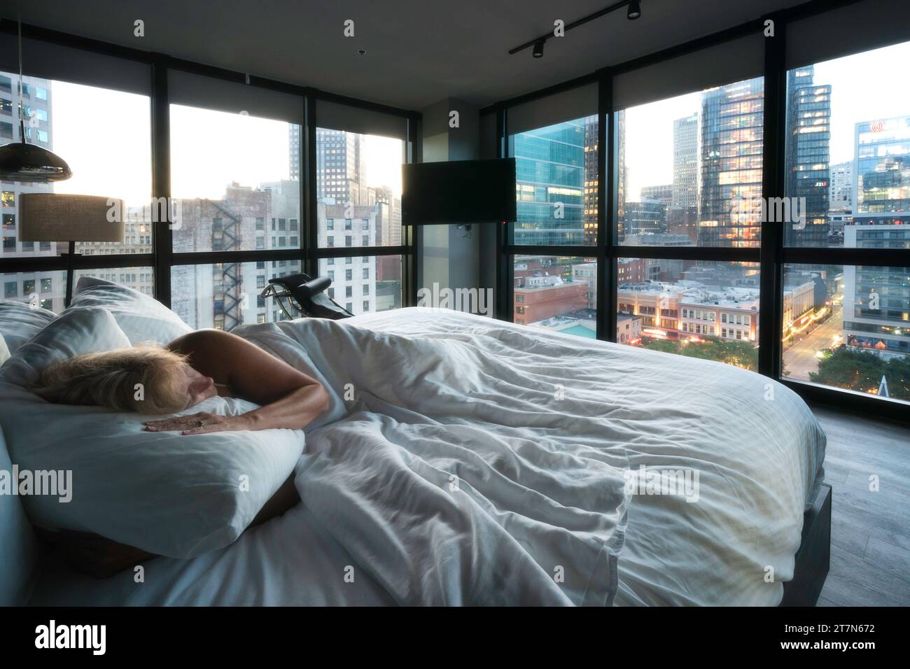 Pittsburgh, Pennsylvanie, États-Unis une femme se réveille avec des vues sur les gratte-ciel du centre-ville vus à travers les fenêtres d'une chambre contemporaine Banque D'Images