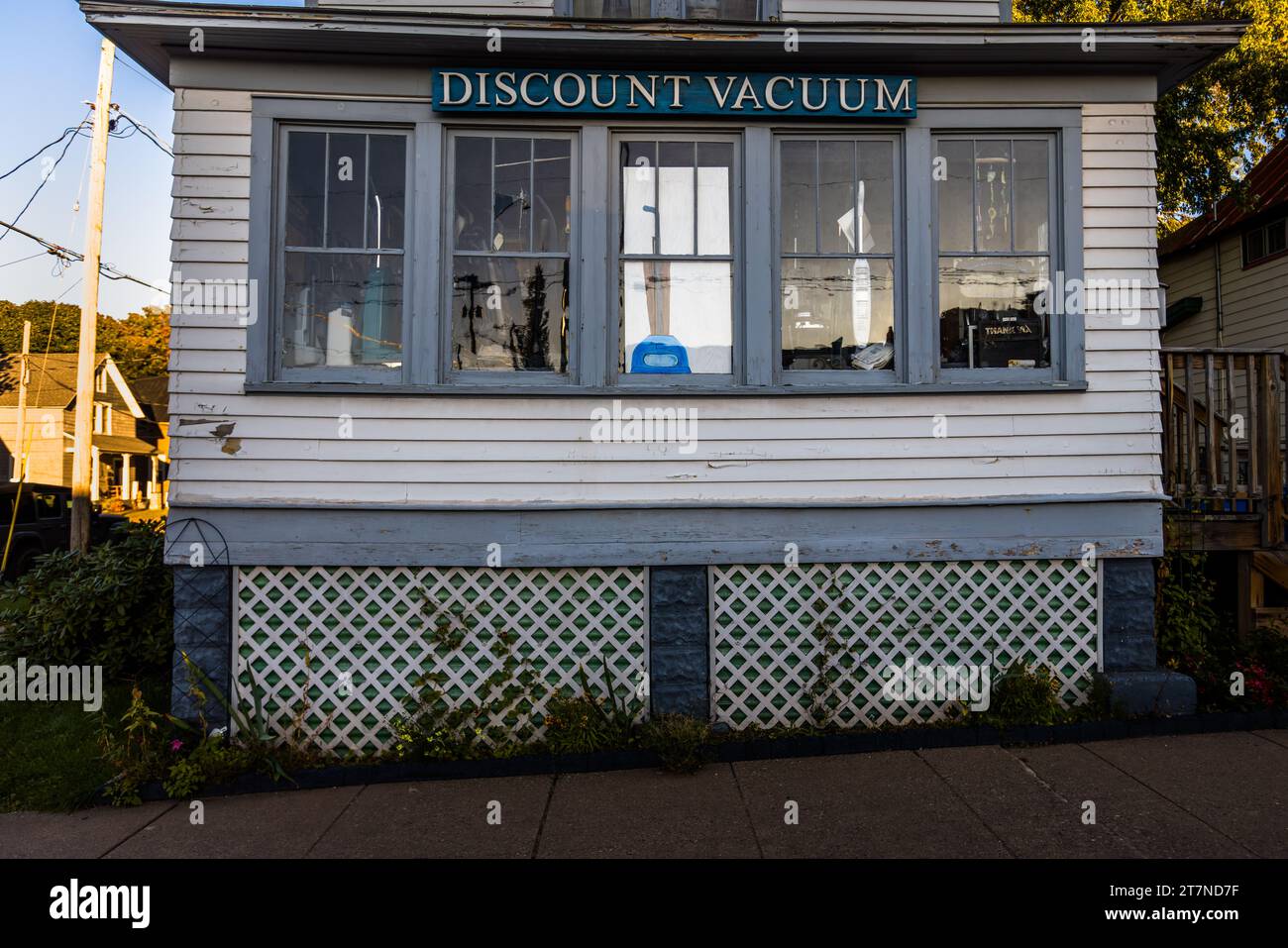 "Discount Vacuum" est écrit en lettres bleues au-dessus de la vitrine d'un magasin vendant des aspirateurs d'occasion, abrité dans un bâtiment à cadre en bois blanc à Marquette, Michigan, États-Unis. Des aspirateurs et des accessoires sont disposés derrière la vitrine, et la façade montre des signes clairs d'usure. Banque D'Images