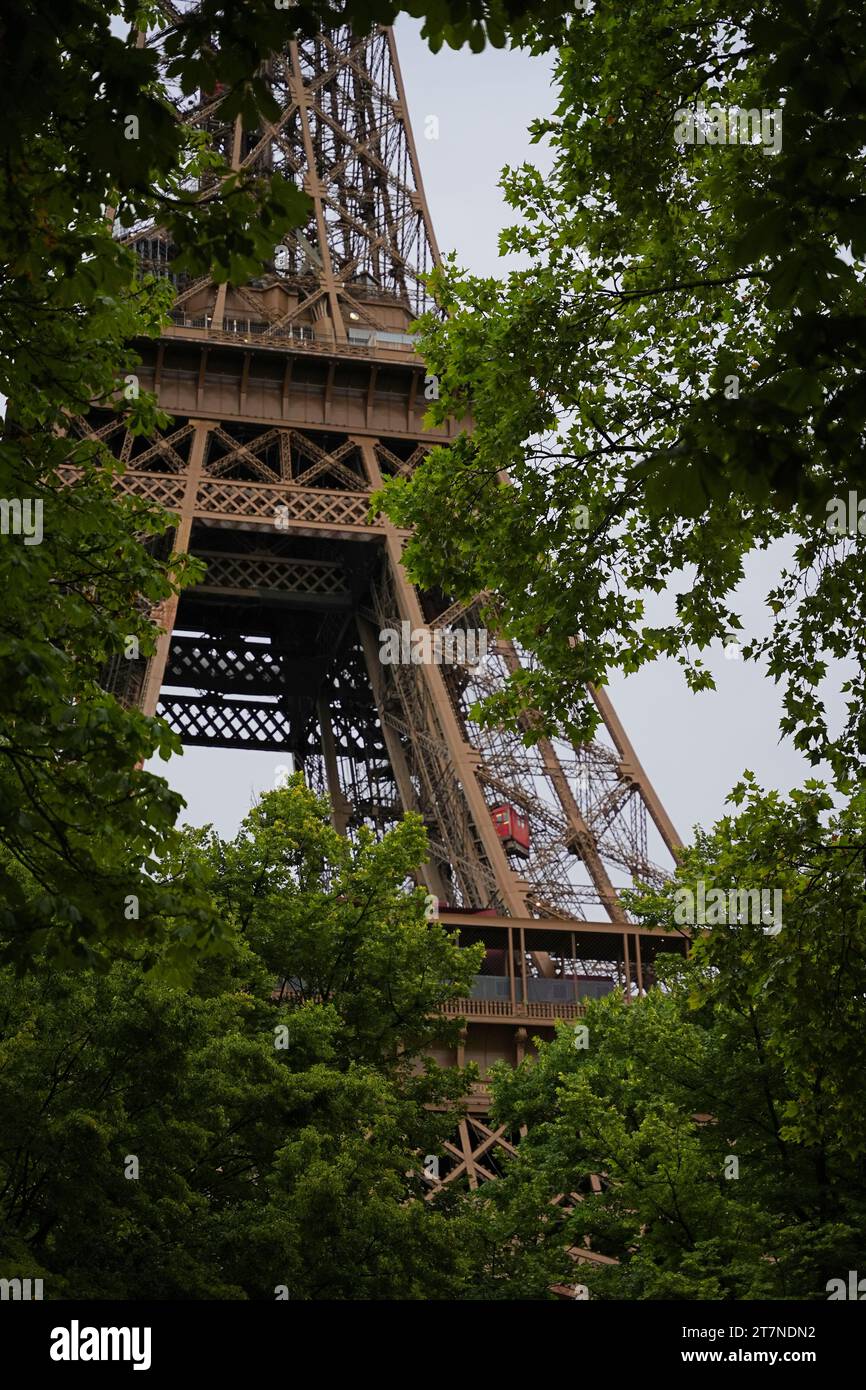 Paris, France - 28 juillet 2023 : vue sur la tour Eiffel à travers des arbres verts avec fond de nuage. Tour Eiffel depuis le champ de Mars. Banque D'Images