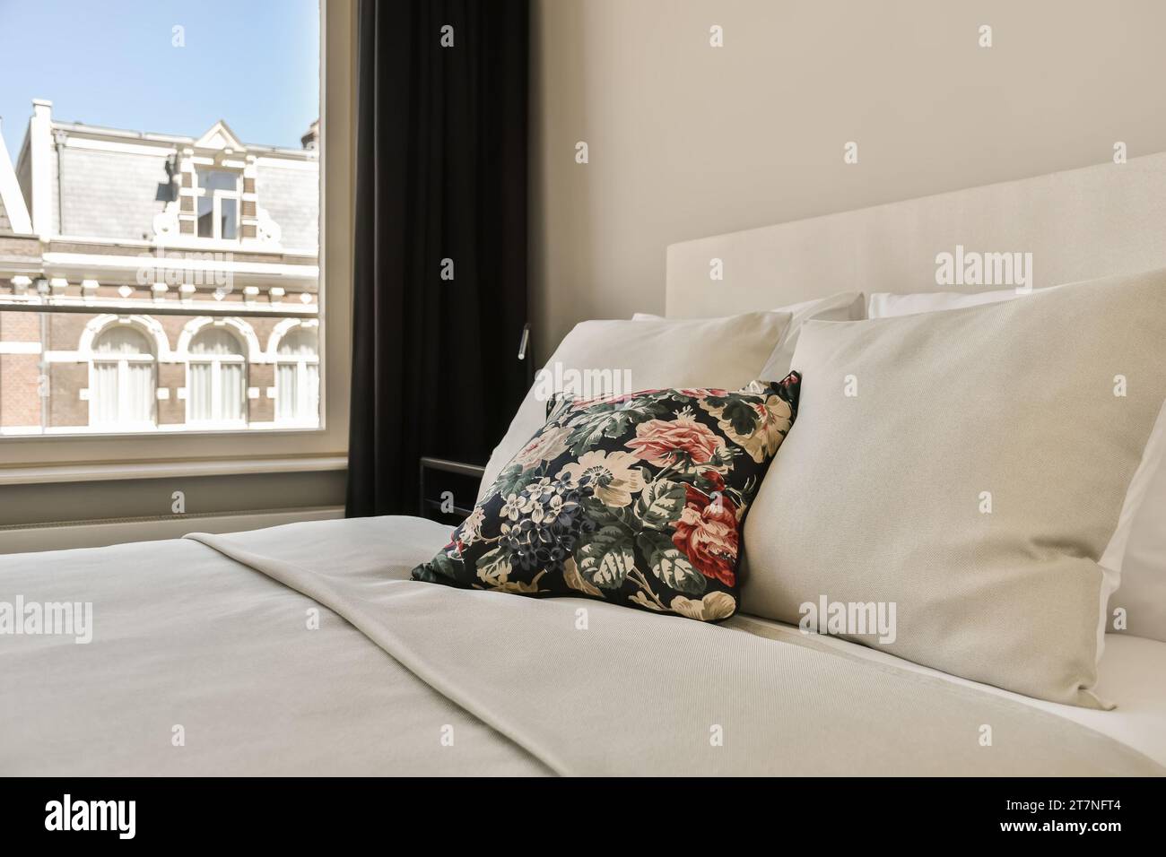 un lit avec des draps blancs et des oreillers devant une grande fenêtre donnant sur la cityscapea Banque D'Images