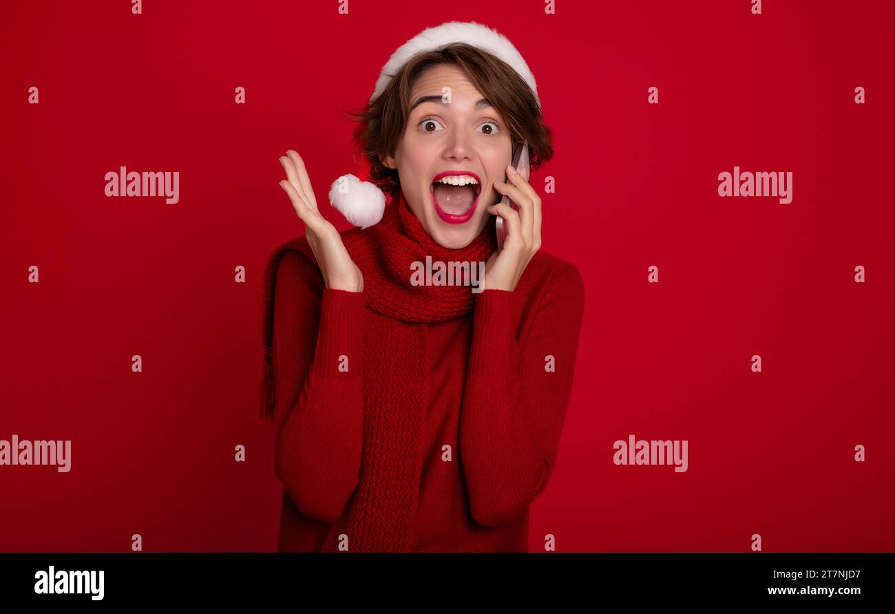 Belle dame excitée dans le chapeau de Santa rouge parle au téléphone avec bien-aimé ou des amis. Joyeux noël. Bonne année. Vacances et célébration Banque D'Images