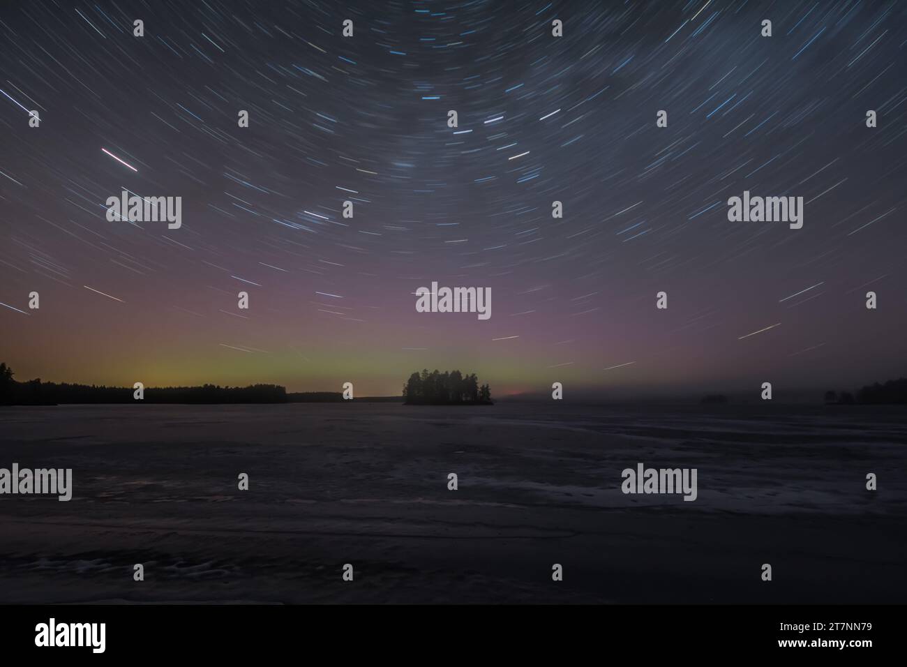 Sentiers étoilés et teinte verte des aurores boréales lointaines au-dessus d'une île boisée dans un lac gelé en hiver en Finlande Banque D'Images