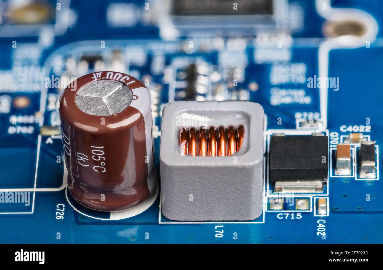 Gros plan de l'inductance, du condensateur électrolytique ou du transistor sur fond de carte flou. Carte de circuit imprimé d'alimentation bleue avec composants électroniques. Banque D'Images