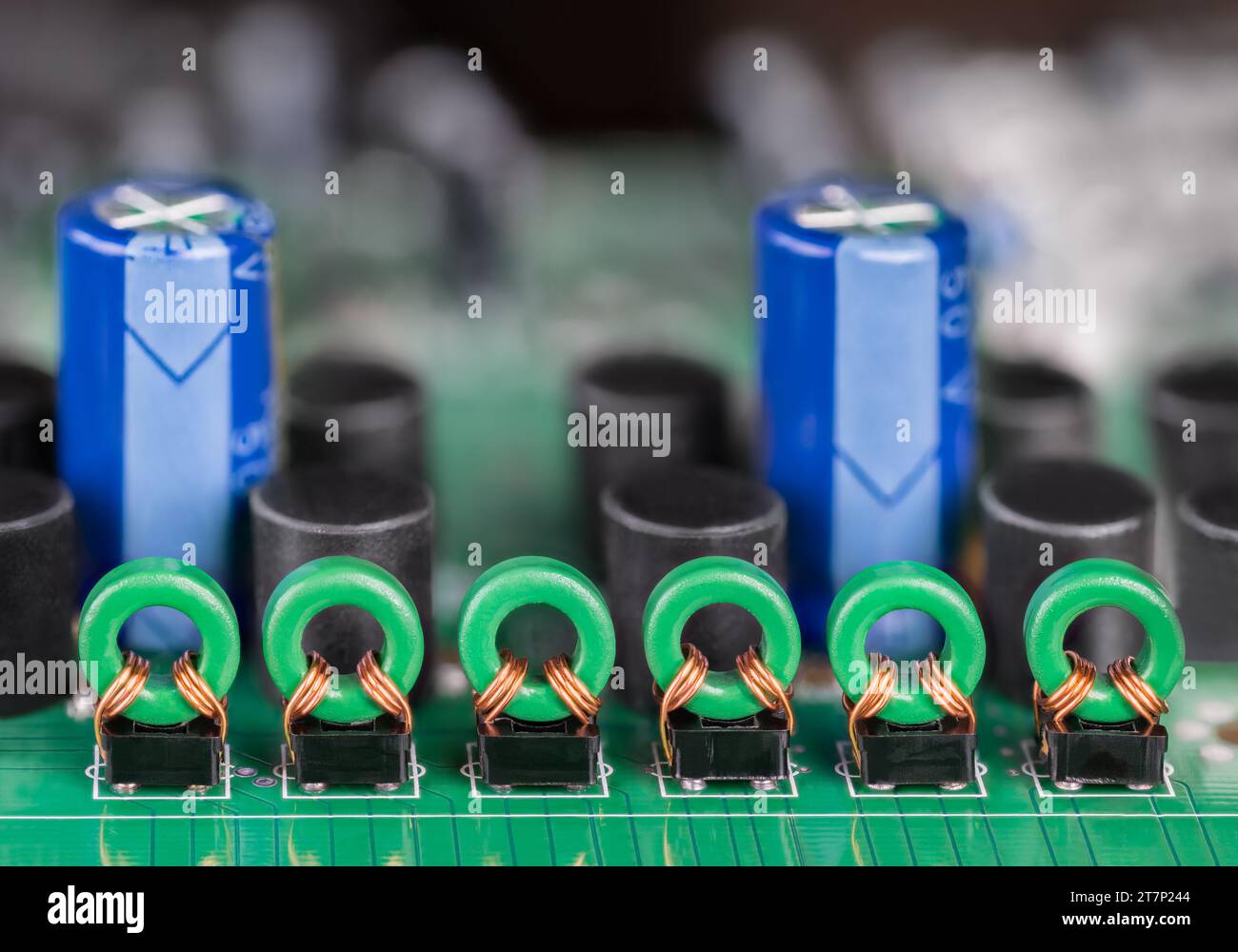 Gros plan des bobines toroïdales et des condensateurs électrolytiques bleus sur PCB vert. Rangée d'inductances de transformateur dans l'isolation galvanique de signal audio ou vidéo. Banque D'Images