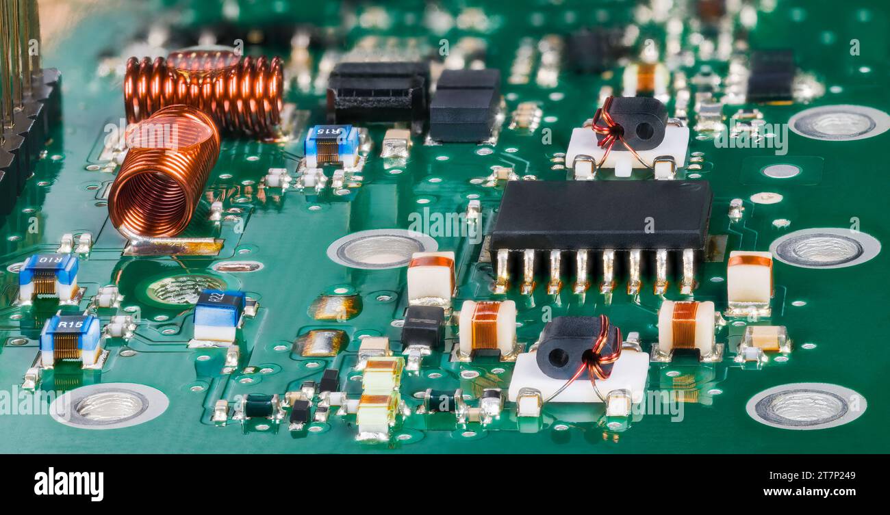 Vue rapprochée de composants électroniques montés en surface dans des circuits radiofréquence de syntoniseur de télévision. Micropuce semi-conducteur et bobines à noyau d'air sur un circuit imprimé vert. Banque D'Images
