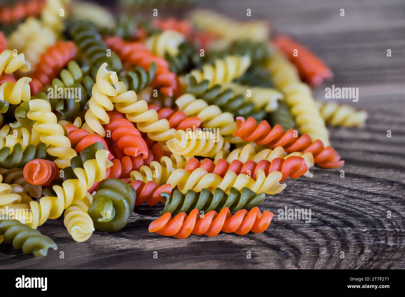 Tas de pâtes fusilli jaunes, rouges ou vertes de forme hélicoïdale sur fond de bois brun. Gros plan un tas de rotini colorés crus de saveur tomate ou épinard. Banque D'Images