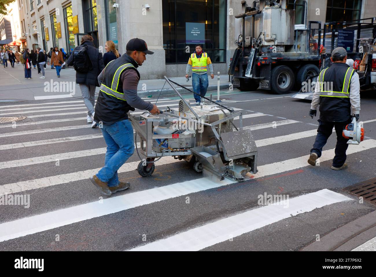 Des travailleurs striant un passage de la ville de New York avec de la peinture époxy thermoplastique et des perles de verre réfléchissantes à l'aide d'un chariot de doublure en aluminium MRL. Banque D'Images