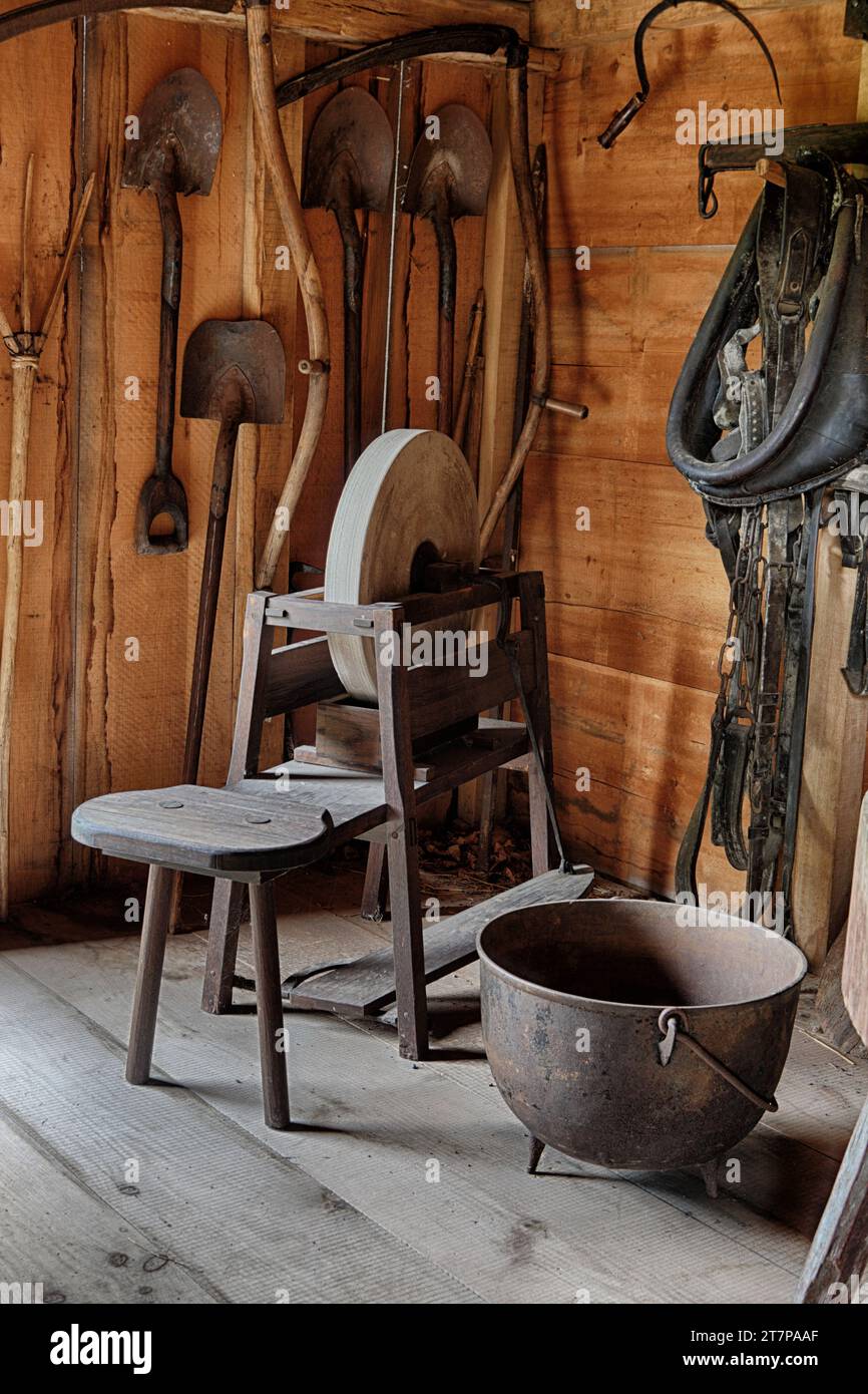 Une meule antique de style pédale exposée dans une grange de reproduction vintage avec d'autres outils du 19e siècle. Banque D'Images