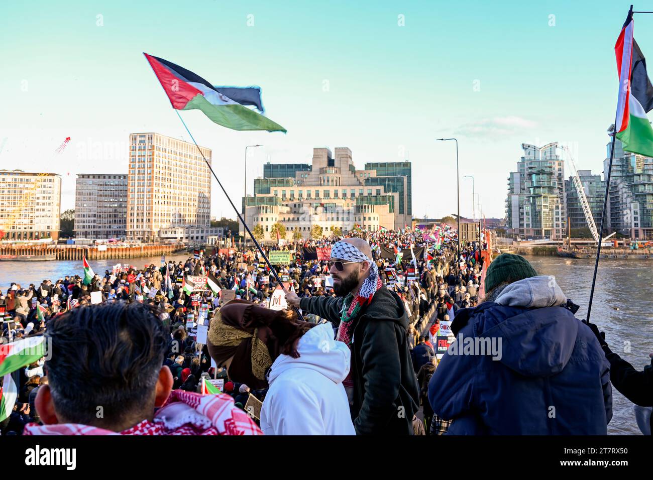 Un homme en bandana agite le drapeau palestinien comme manifestants lors d'une marche pour la Palestine à travers le pont Vauxhall dans le centre de Londres sous l'œil vigilant du bâtiment MI6 Banque D'Images