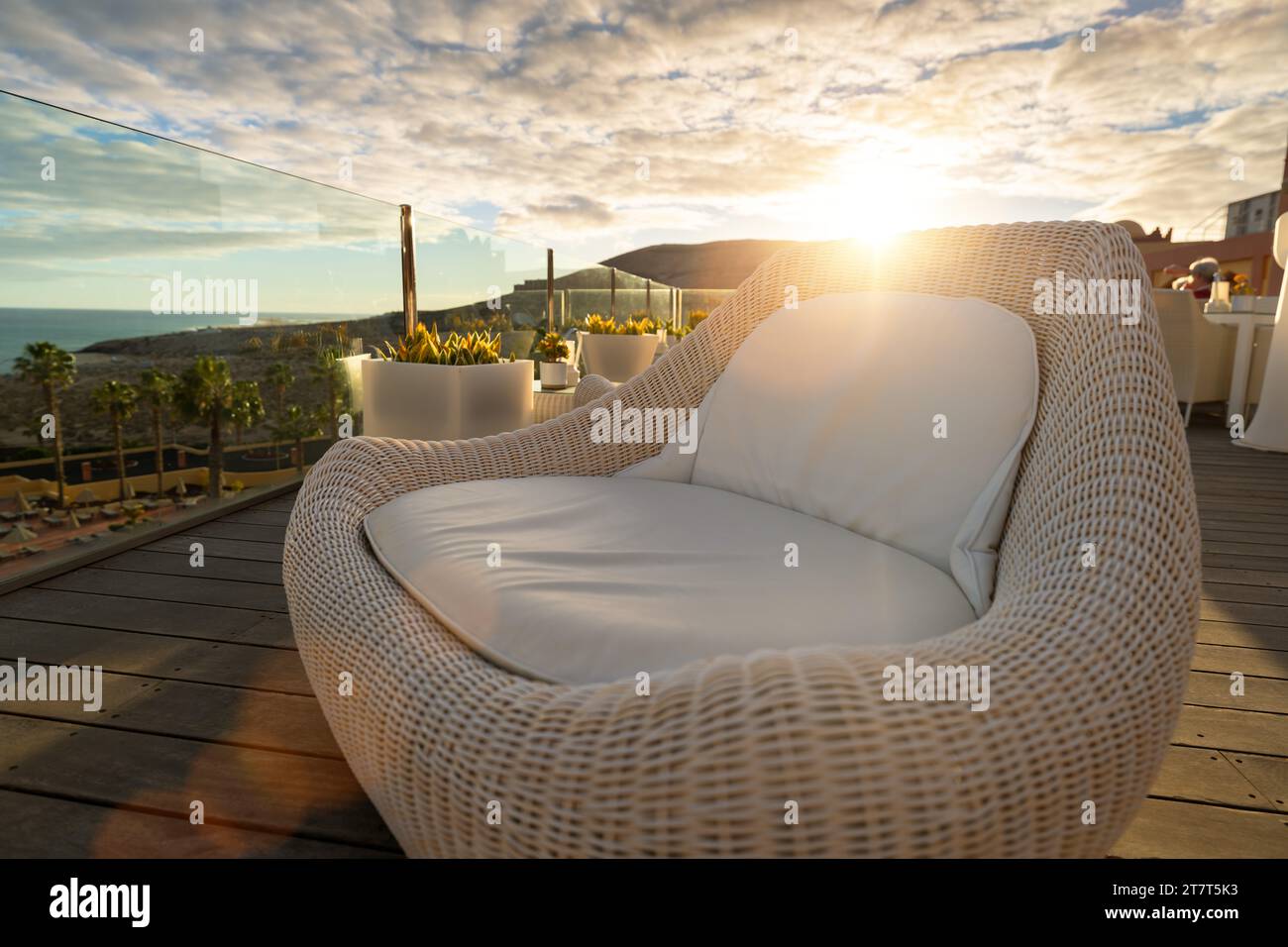 Chaise longue en osier sur la terrasse de l'hôtel au coucher du soleil avec vue sur l'océan et la montagne Banque D'Images