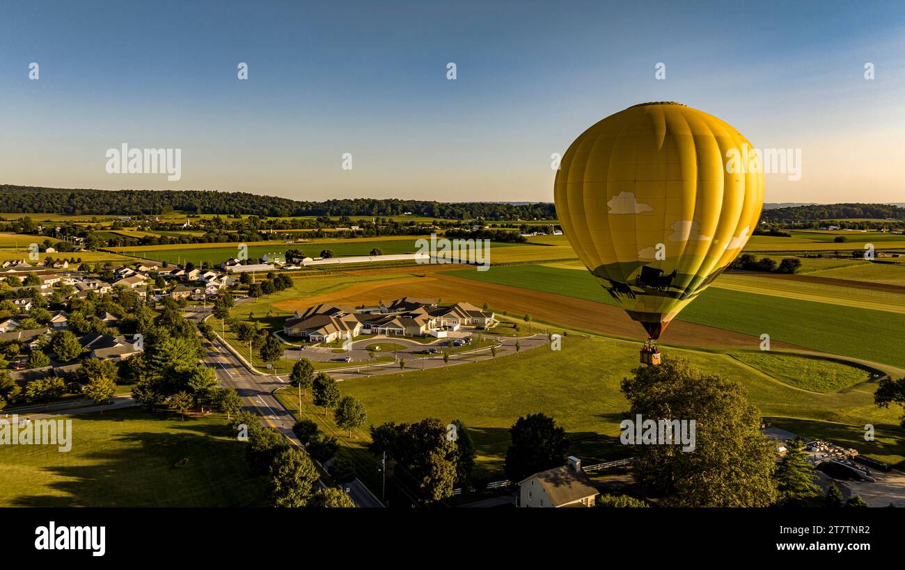 Une vue aérienne sur une montgolfière jaune flottant au-dessus d'une communauté de campagne, par une belle journée d'été Banque D'Images