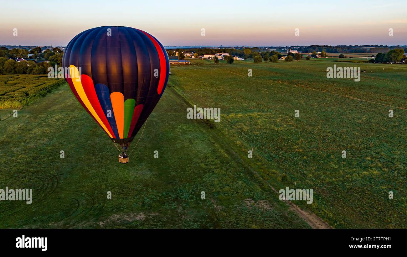 Vue aérienne d'une montgolfière à rayures noires flottant au-dessus des champs et des terres agricoles en Amérique rurale par un matin d'été ensoleillé. Banque D'Images