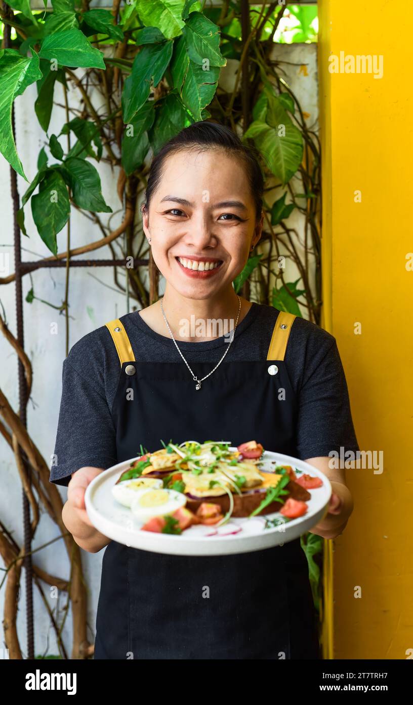 Jeune serveuse vietnamienne tenant une assiette avec du pain grillé au poulet Banque D'Images