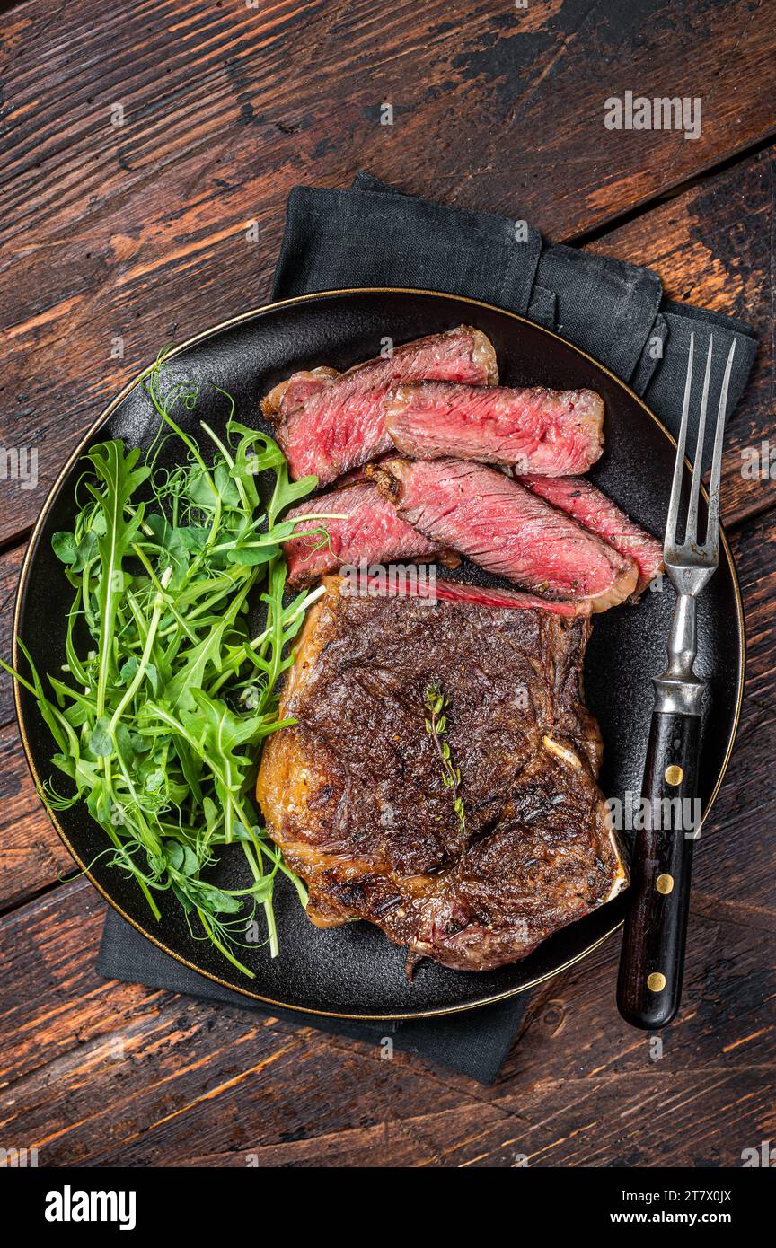 Steak de viande de bœuf Wagyu New York grillé au barbecue ou steak de stripline dans une assiette avec salade. Arrière-plan en bois. Vue de dessus. Banque D'Images