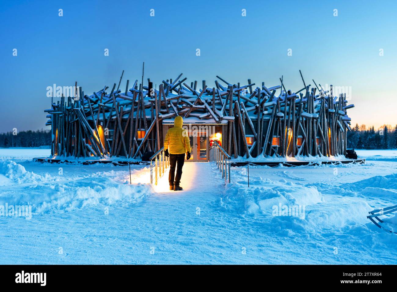 Personne se tient sur le pont reliant le bâtiment principal de l'hôtel illuminé Arctic Bath fait de rondins, heure du crépuscule, Harads, Laponie suédoise Banque D'Images