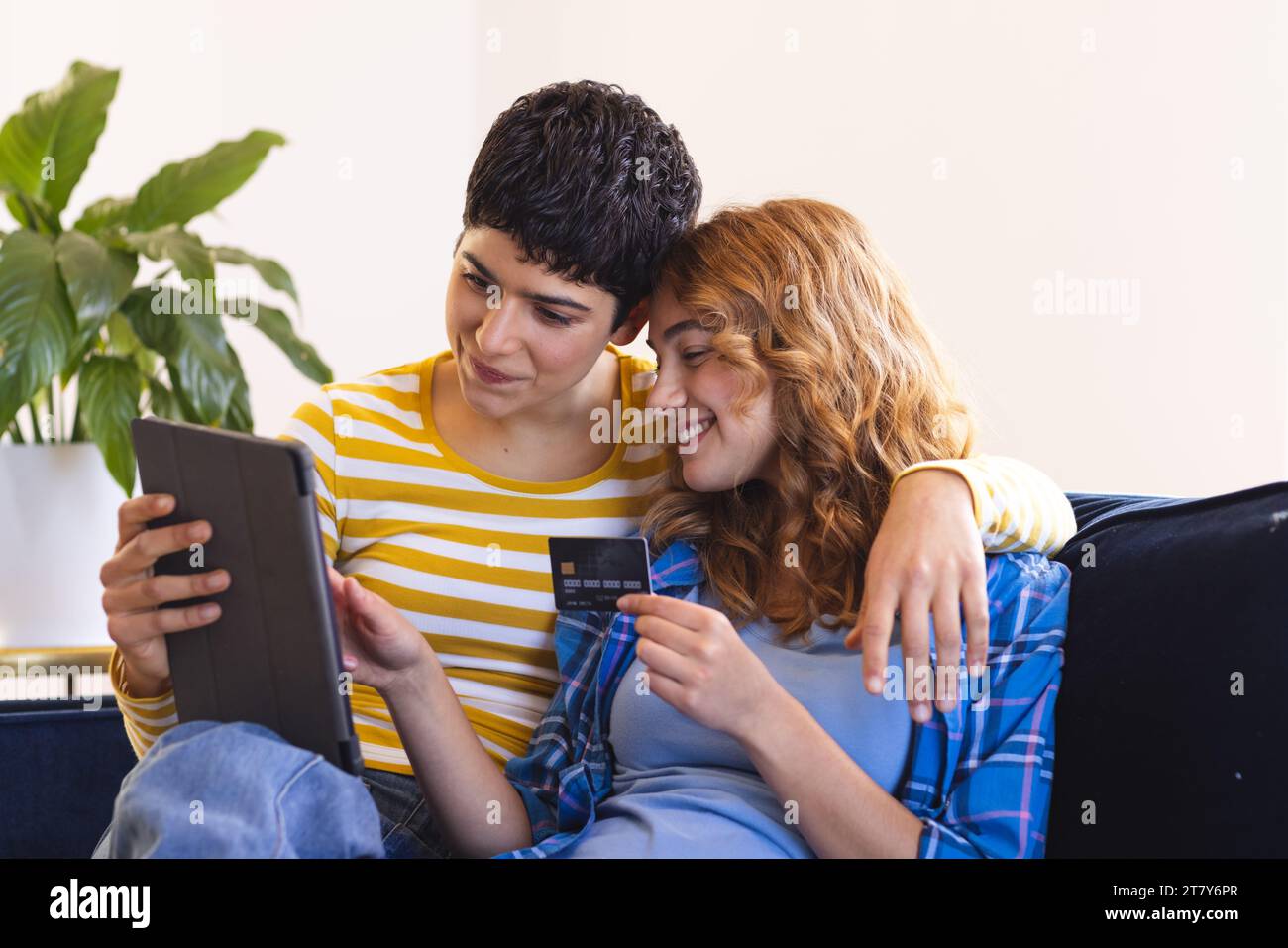 Heureux couple biracial lesbienne sur le canapé shopping en ligne avec tablette et carte de crédit Banque D'Images