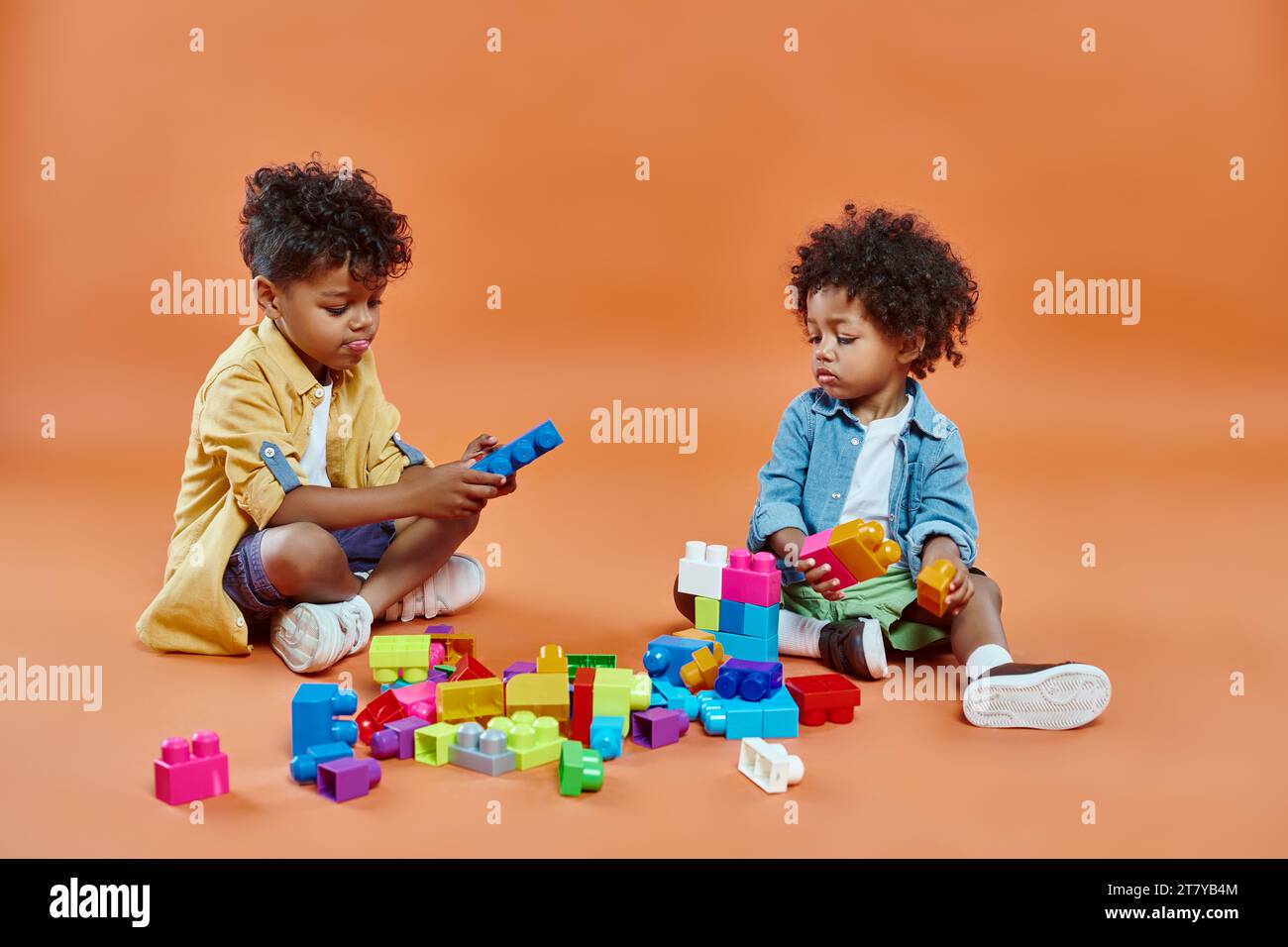 mignon garçon afro-américain frères et sœurs en tenue décontractée assis et jouant des blocs de construction sur orange Banque D'Images