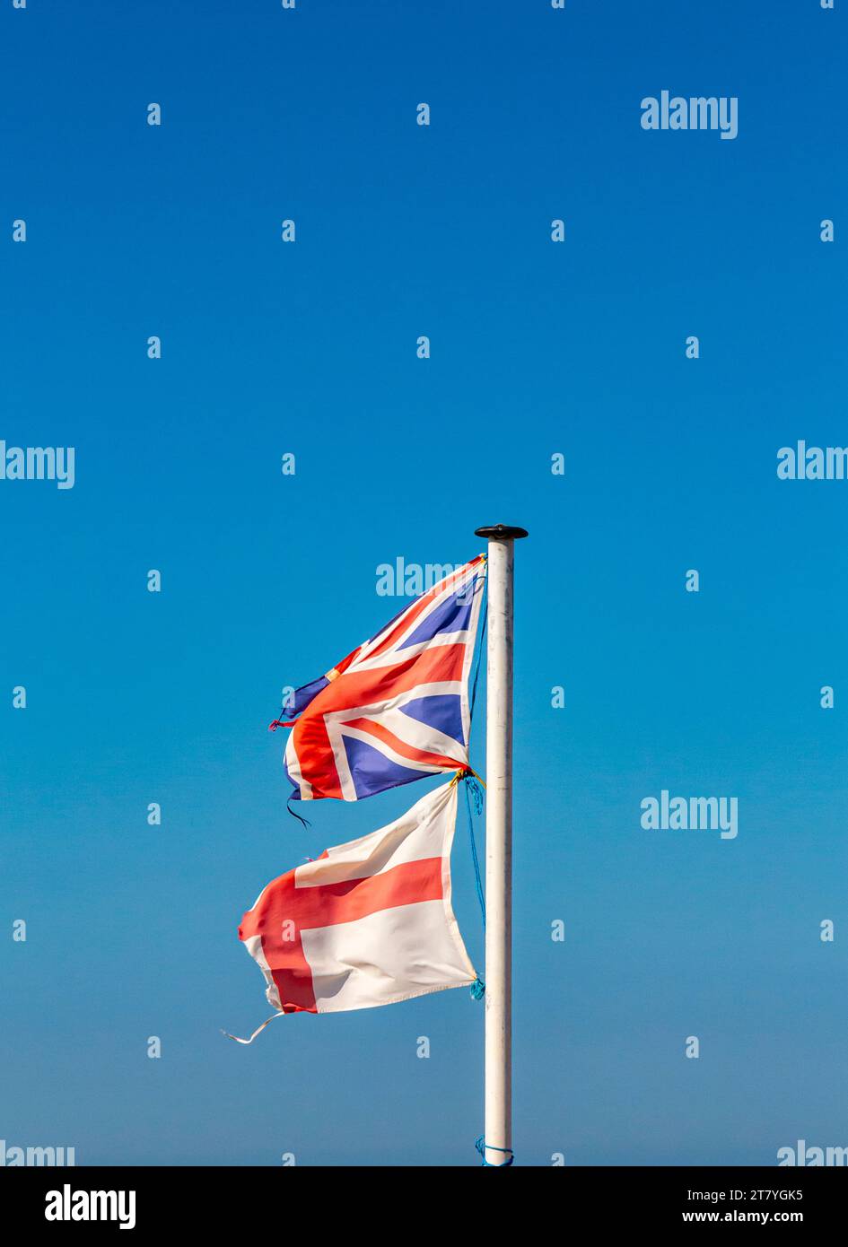 Drapeaux de l'Angleterre et de l'Union Jack en lambeaux et déchirés sur un poteau de drapeau avec ciel bleu en arrière-plan. Banque D'Images