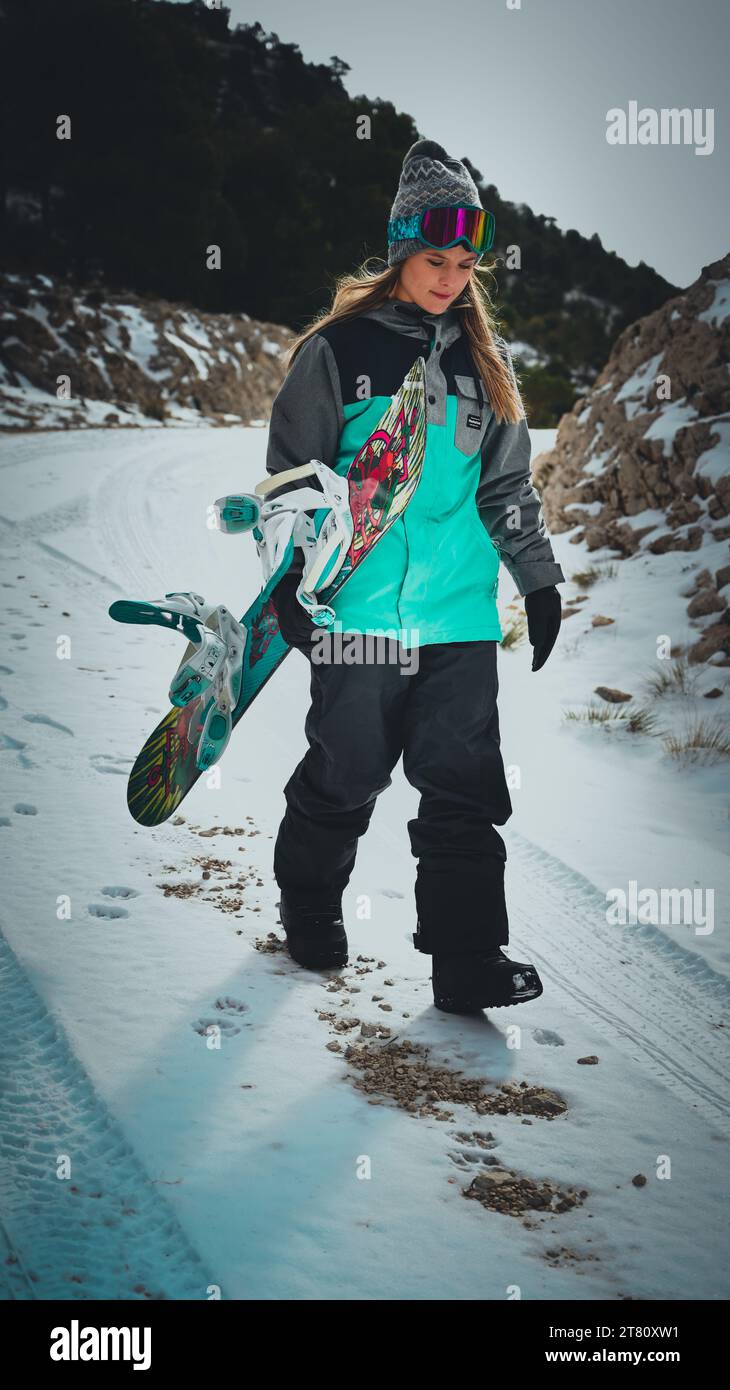 Une jeune femme en tenue de snowboard verte et noire glisse sur une pente de montagne enneigée Banque D'Images