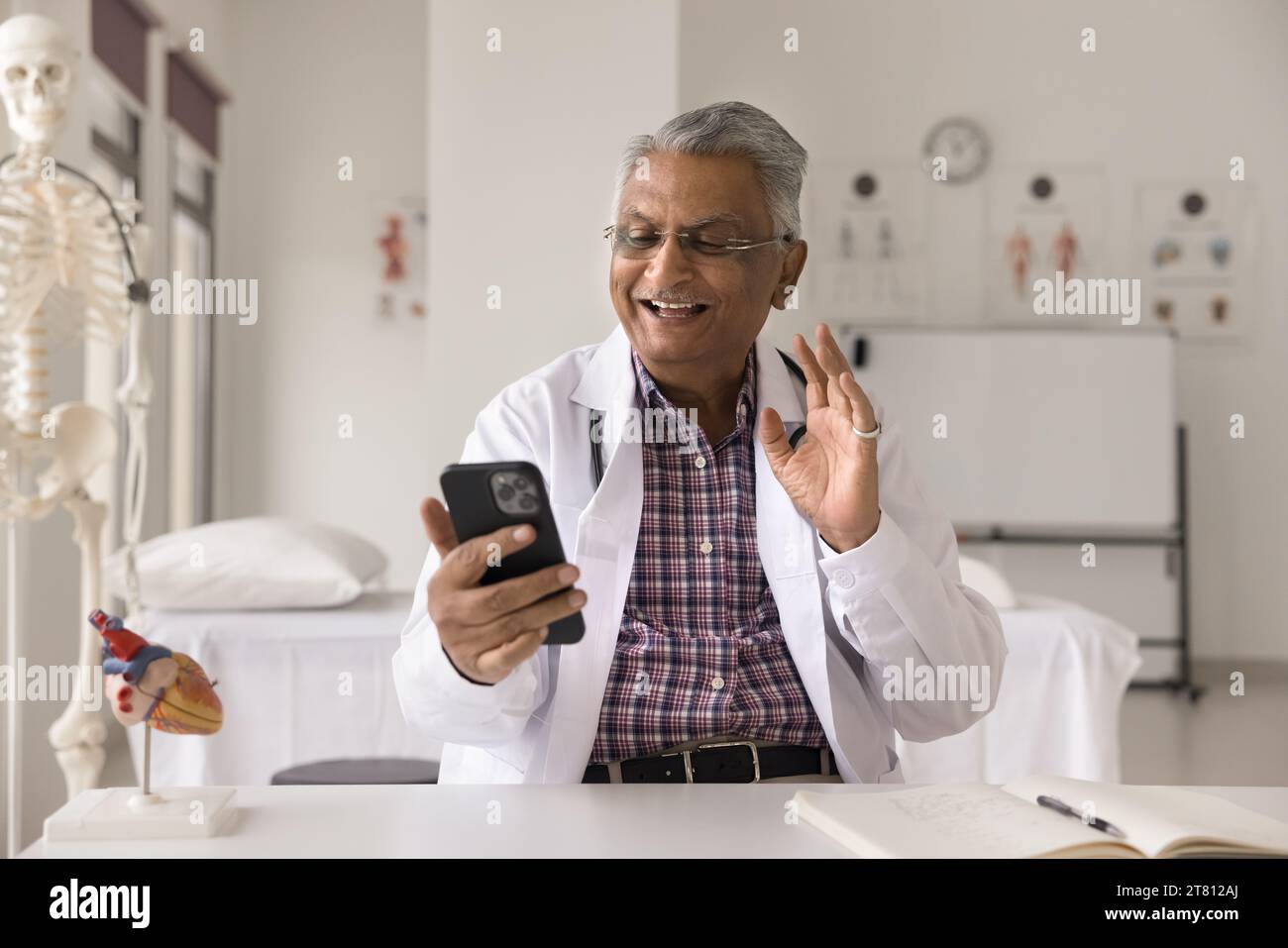 Joyeux homme médecin indien senior donnant consultation en ligne sur smartphone Banque D'Images