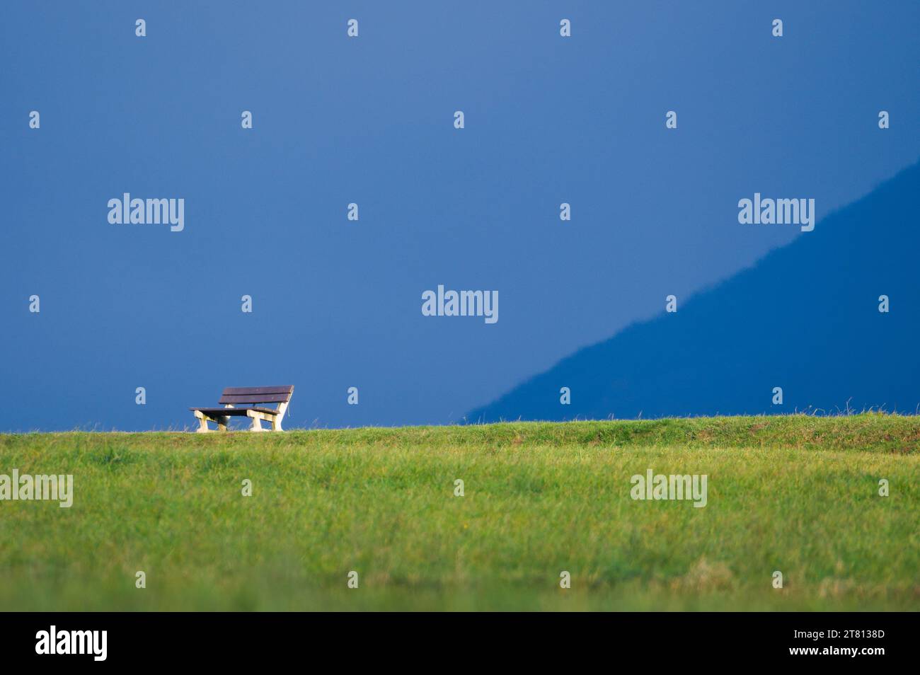 Banc vide solitaire à l'horizon dans la nature. Concept de solitude. Isolé sur fond bleu. Espace négatif pour le placement du texte. Banque D'Images