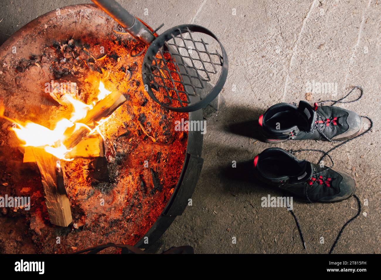 Une paire de chaussures de randonnée se dessèche par un feu avec quelques bûches brûlant à l'intérieur d'une cabane dans le nord de la Finlande Banque D'Images