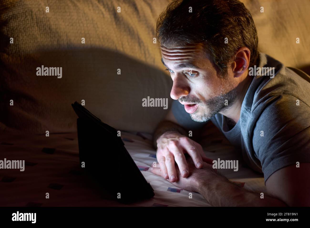 Jeune homme de 30 ans couché dans son lit la nuit tout en regardant
