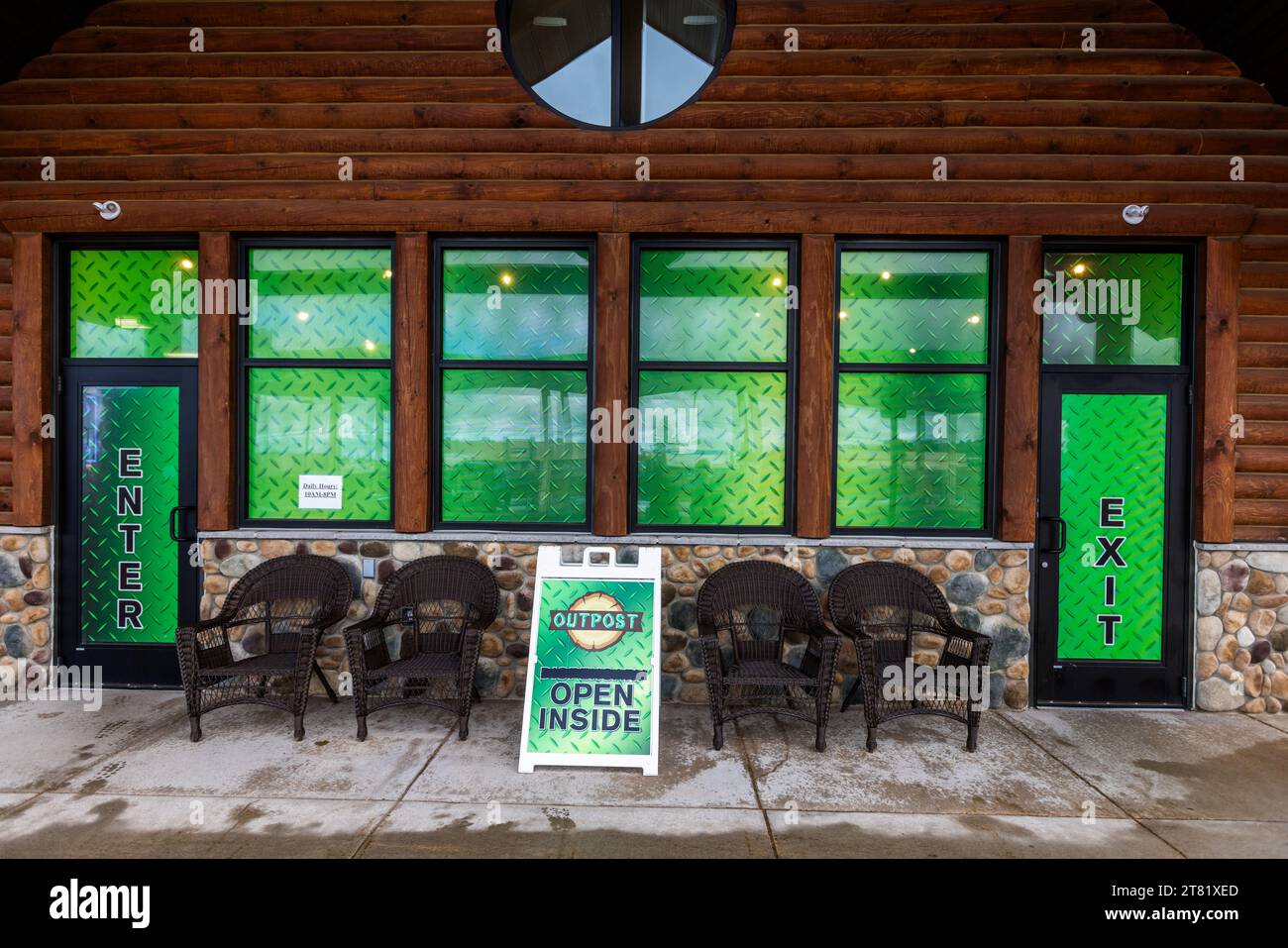 Des fenêtres teintées de vert et une porte marquée „Enter“ forment l’entrée d’Outpost Marquette, un détaillant officiel de cannabis dans le township de Marquette, Michigan, États-Unis. Un panneau indicateur portant l’inscription „Open Inside“ pointe vers la surface de vente ouverte. Banque D'Images