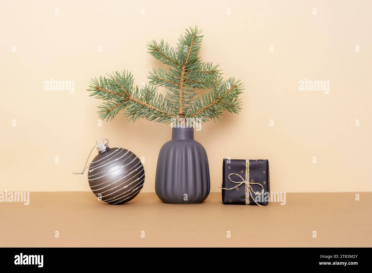 Branche d'épicéa dans un vase en céramique, boîte cadeau et boule de Noël sur table beige. Concept de Noël minimal. Banque D'Images