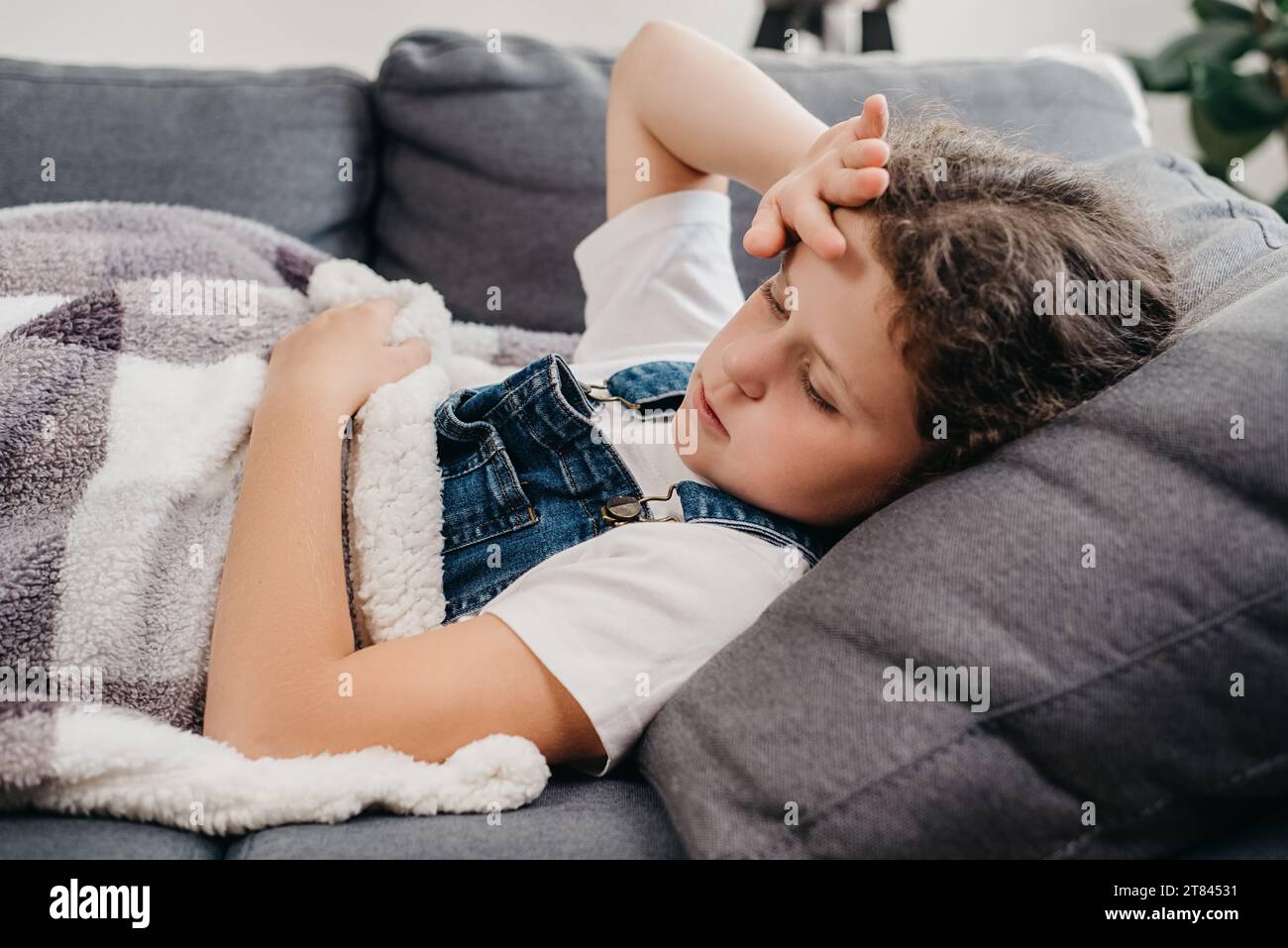 Gros plan d'une petite fille malade en mauvaise santé couchée seule sur un canapé sous une couverture dans le salon à la maison. Contrarié petit enfant caucasien a de la fièvre. Concept de Banque D'Images