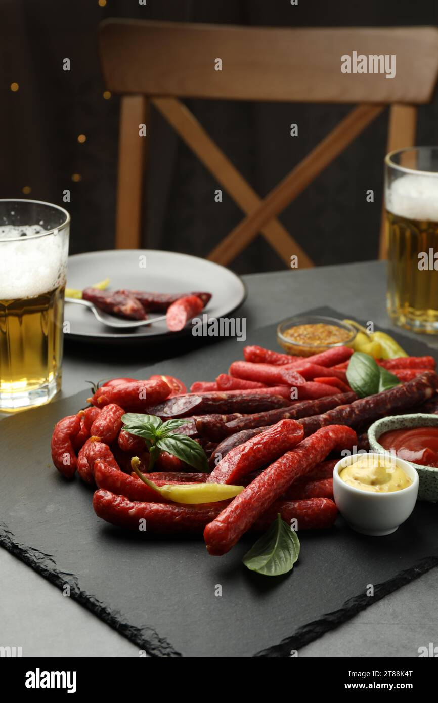 Différentes fines saucisses fumées sèches, sauces et verres de bière sur la table grise Banque D'Images