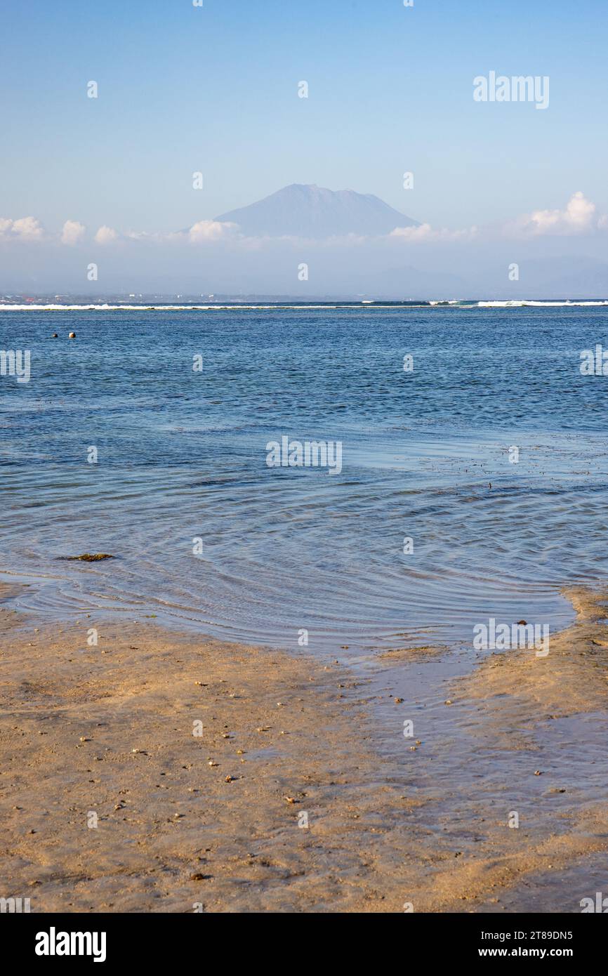 Plage de Sanur. Temple dans la mer calme. Petites vagues le matin. Plage de sable sur l'île de rêve de Bali. En arrière-plan le volcan Mont Agung Banque D'Images