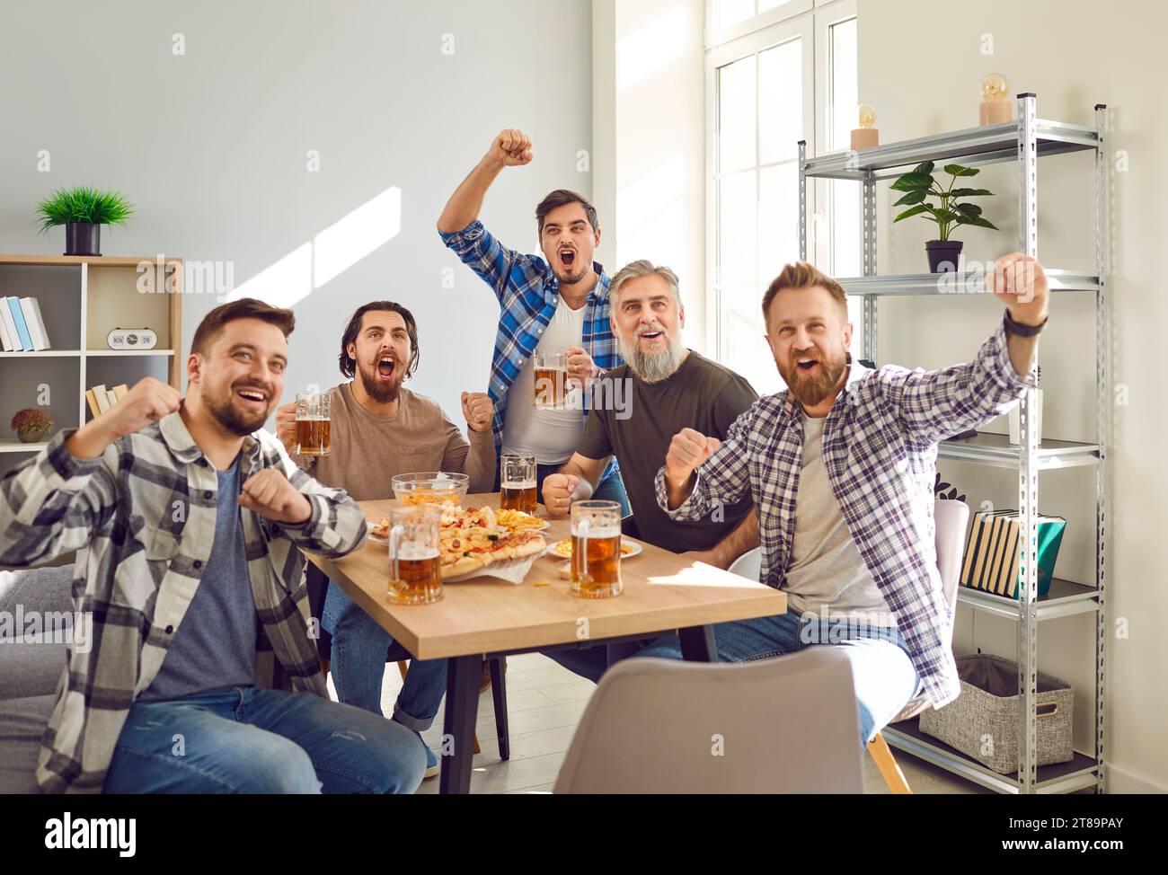 Groupe d'amis excités regardant le match de football à la télévision à la maison avec de la bière et des collations. Banque D'Images