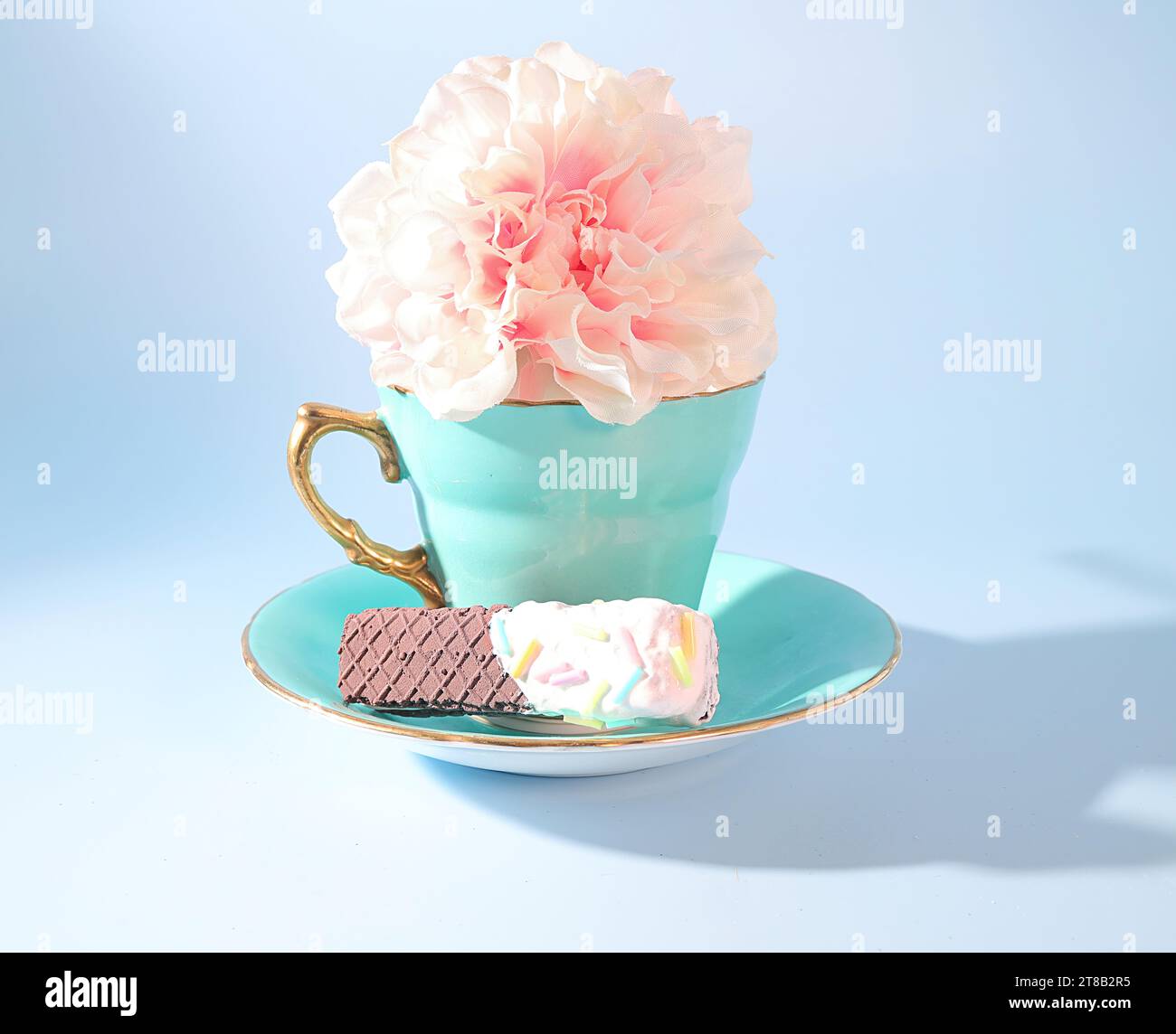 Une célébration du thé au printemps : une tasse de thé vert pastel avec poignée en or, une fleur rose et un biscuit au chocolat Wafer avec des vermicelles colorées Banque D'Images