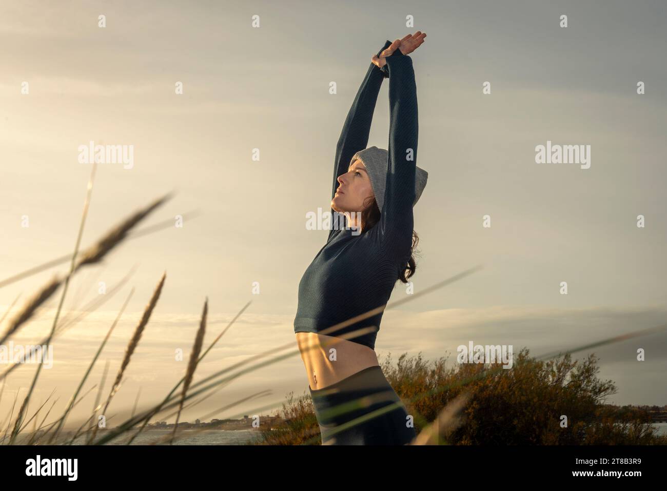Femme en forme, sportive faisant un étirement du bras à l'extérieur au lever du soleil. Banque D'Images