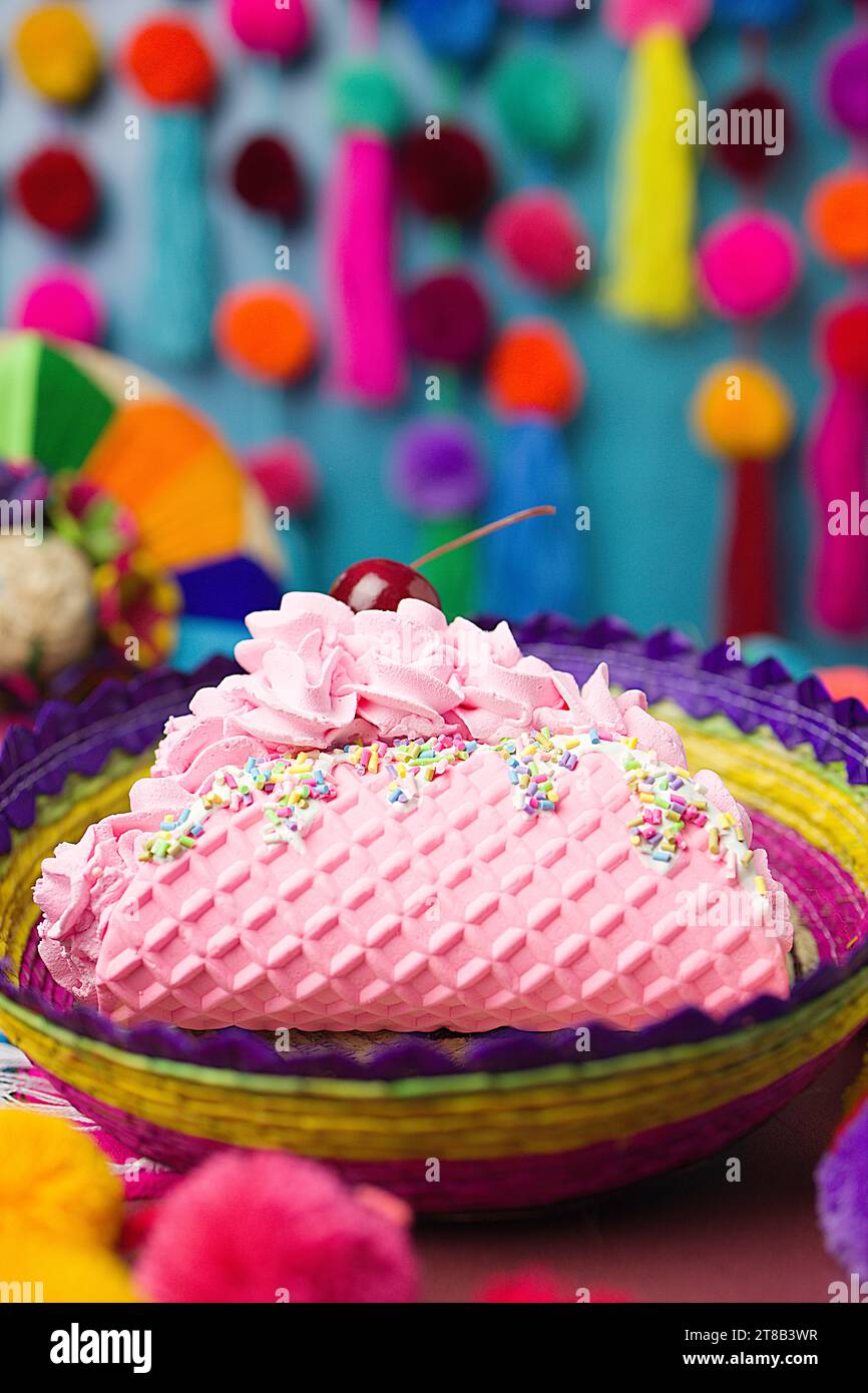 Dessert au Taco à la crème glacée rose avec des prinkles, des fruits de cerise, de la crème fouettée dans un panier tissé à la main coloré sur un fond festif de guirlande de pompon Banque D'Images